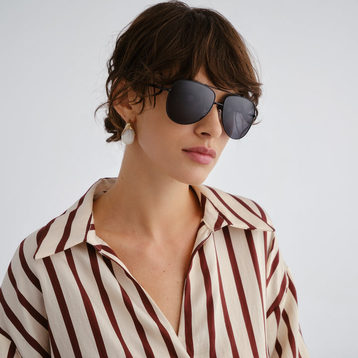 Woman wearing sunglasses and a striped shirt against a plain background