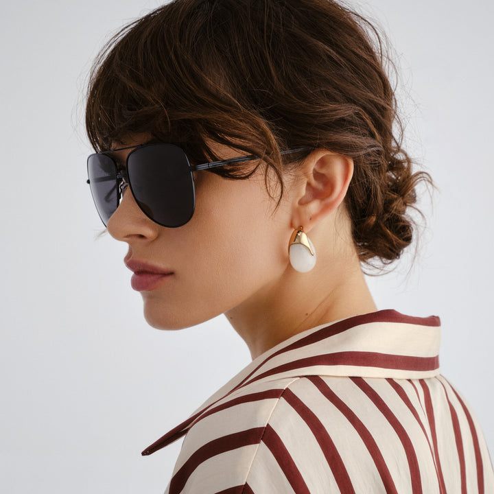 Woman wearing sunglasses and a striped shirt with a plain background