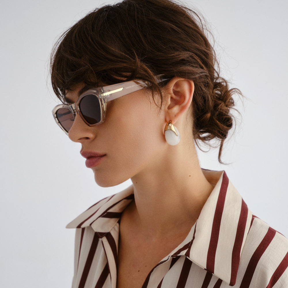 Woman wearing sunglasses and a striped shirt with a neutral background