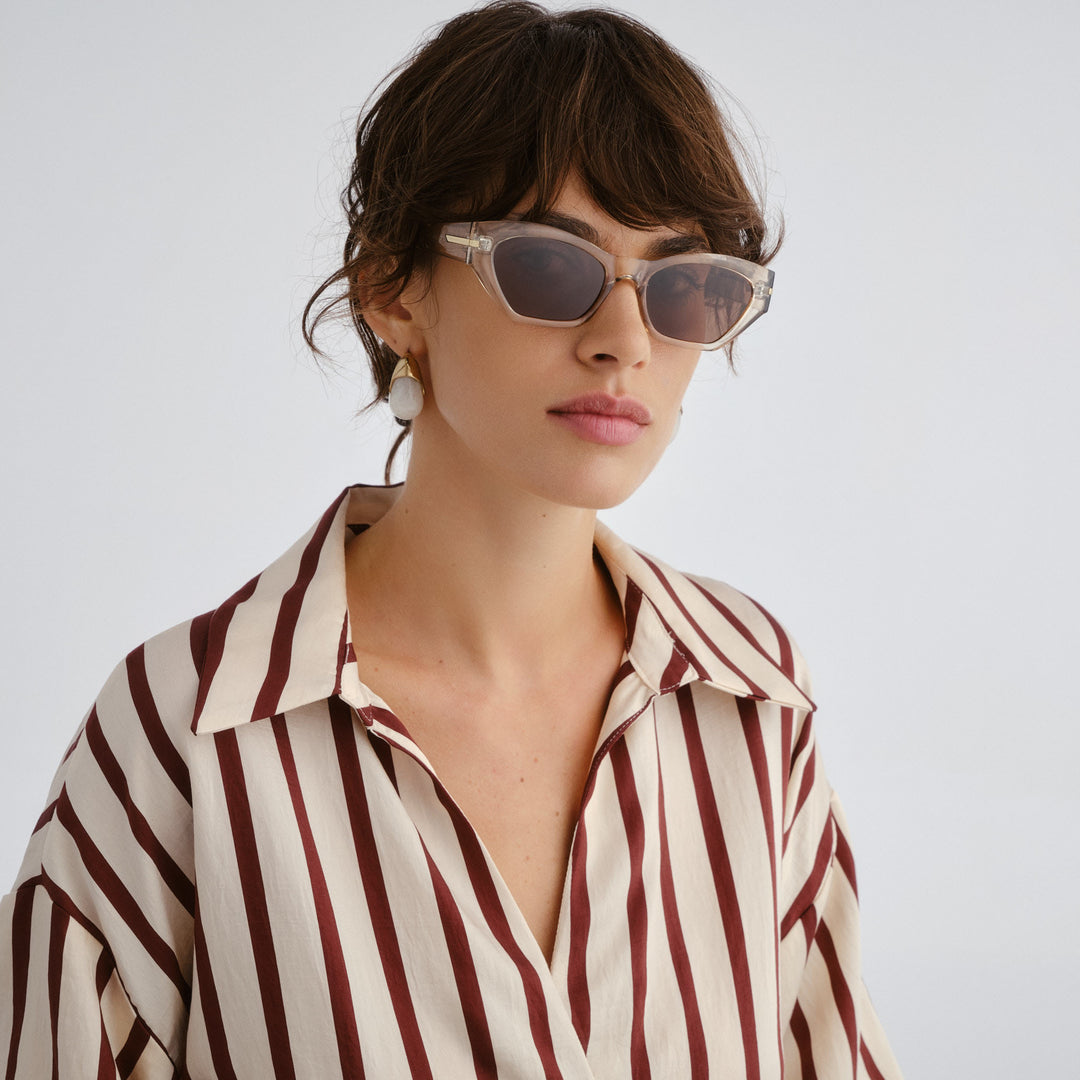 Woman wearing sunglasses and a striped shirt against a plain background