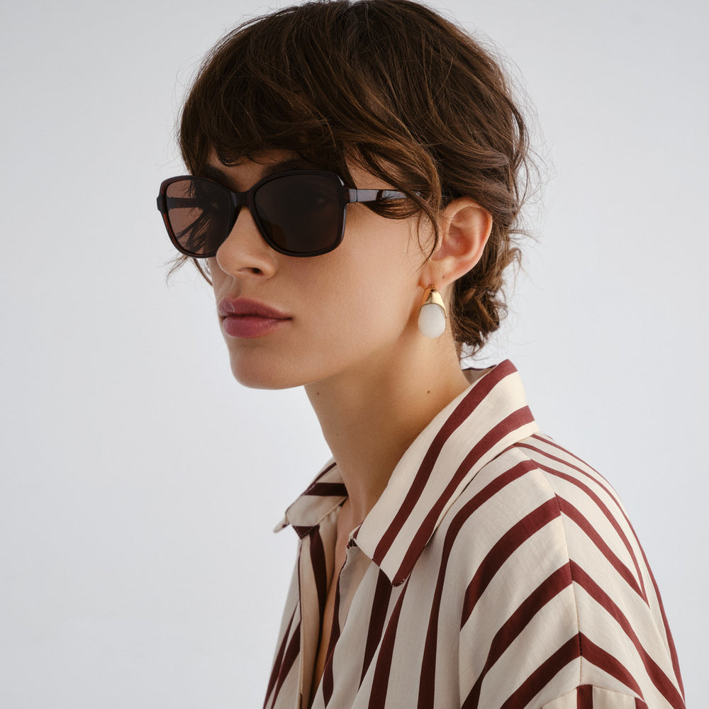Woman wearing sunglasses and a striped shirt with a plain background