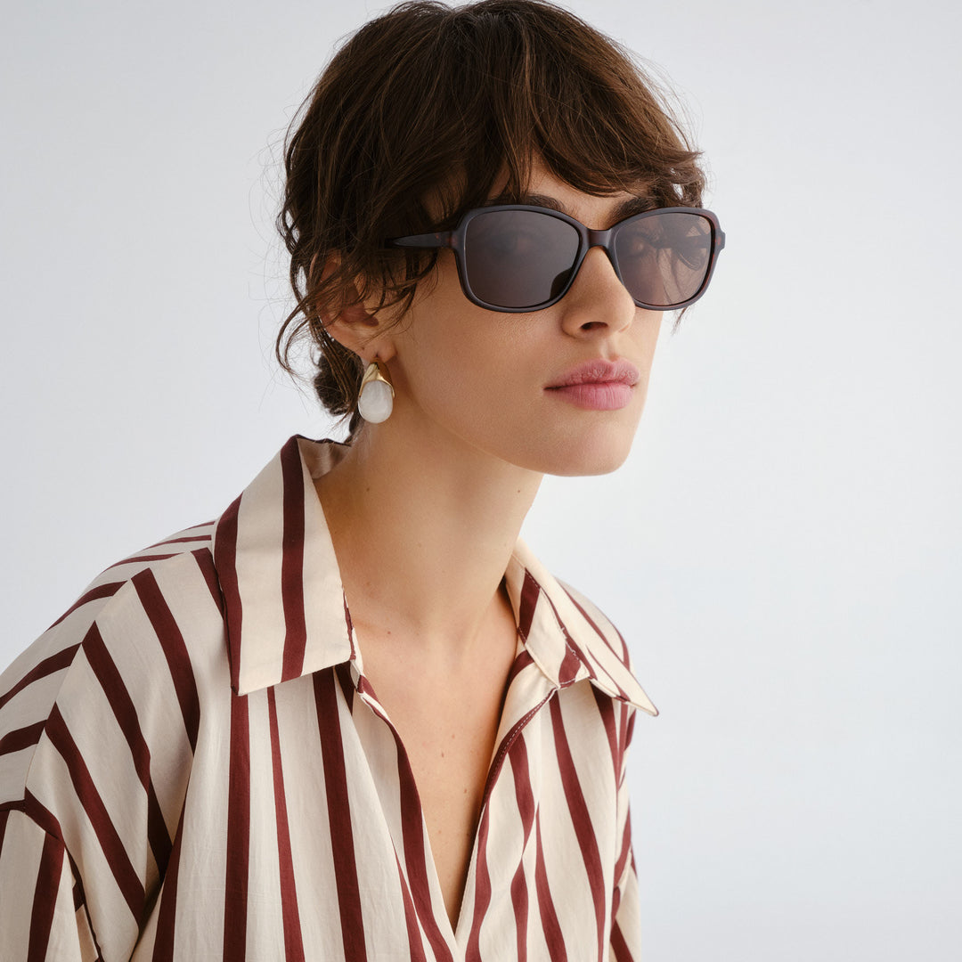 Woman wearing sunglasses and a striped shirt against a plain background