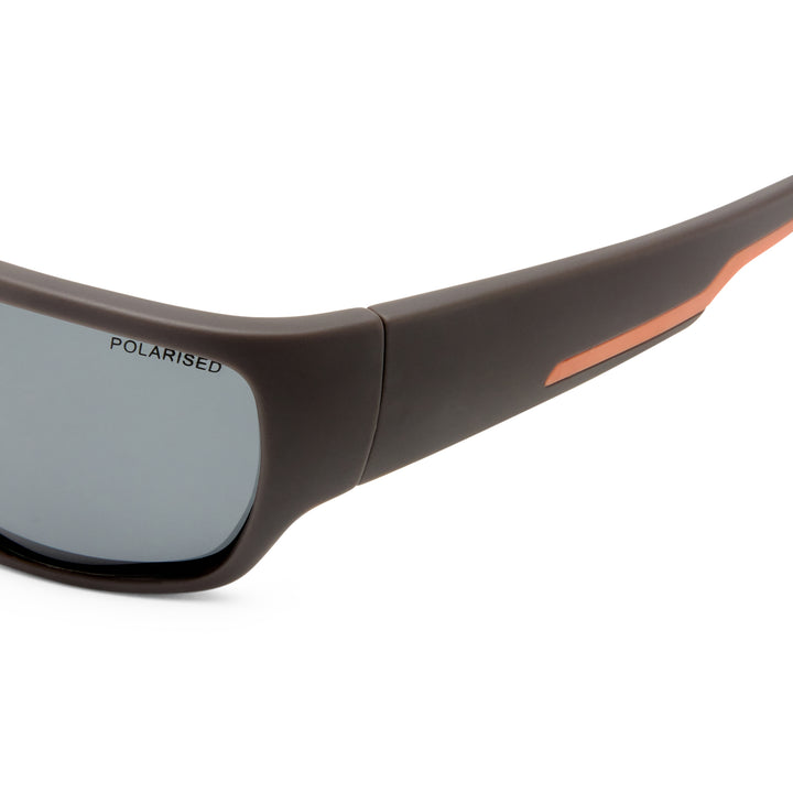 Close-up of a pair of sunglasses with a matte dark brown frame, a gray polarised lens, and a thin orange accent line on the temple arm, shown against a white background.