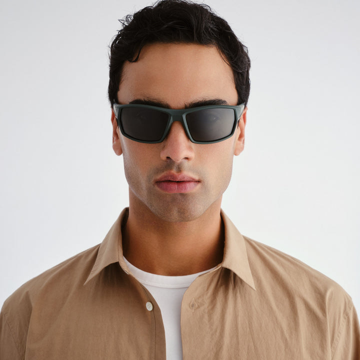 Man wearing dark sunglasses and a beige shirt against a white background