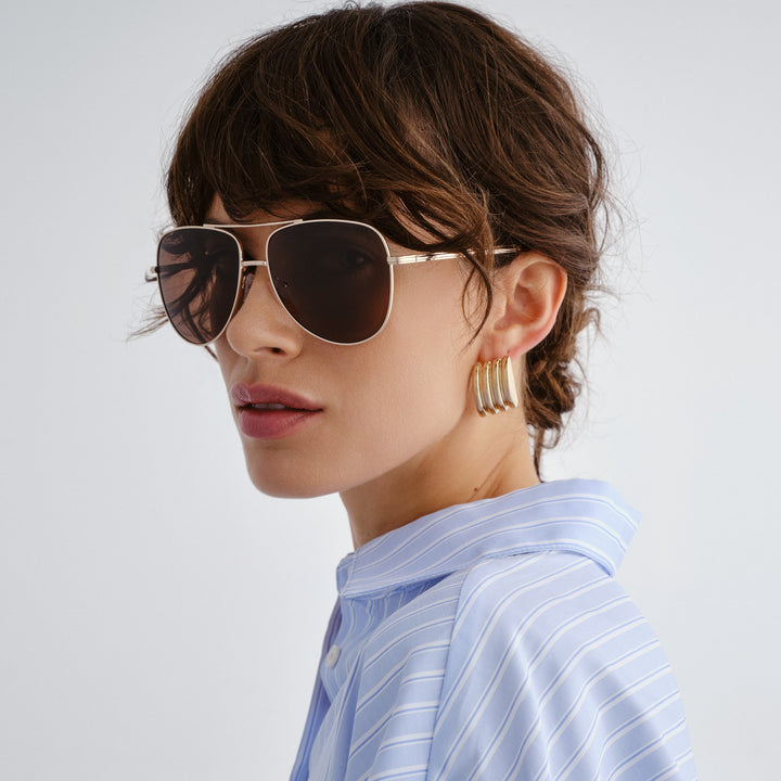 Woman wearing sunglasses and gold earrings with a light gray background