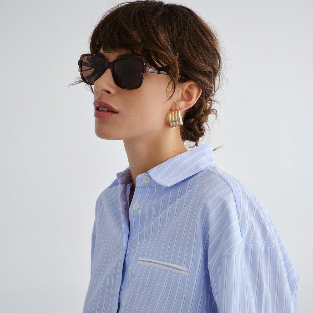 Woman wearing a light blue striped shirt and sunglasses on a plain background