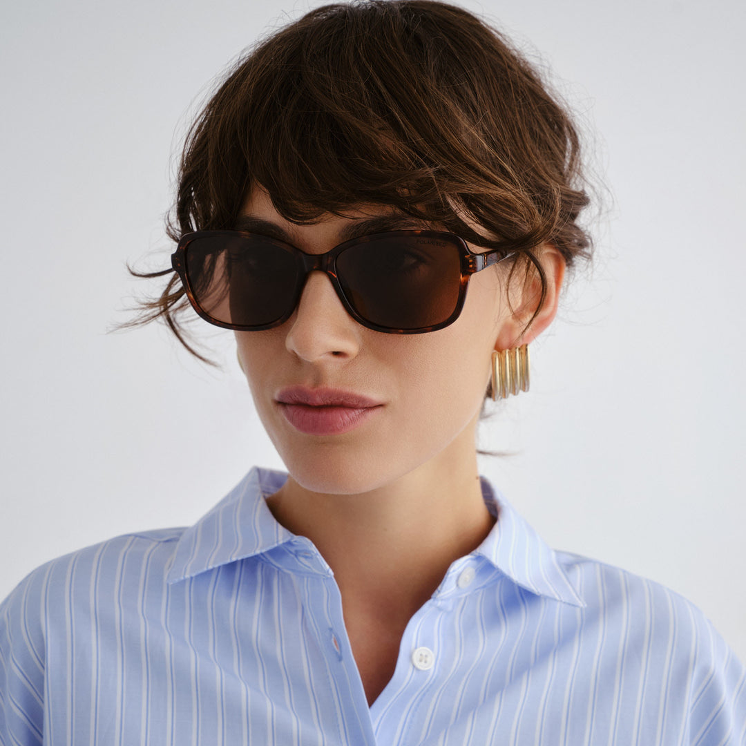 Woman wearing sunglasses and a light blue striped shirt against a white background