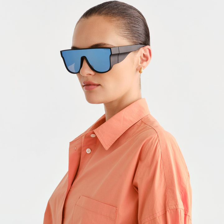 Woman wearing black large sunglasses with blue lens, angled showing wide coverage 