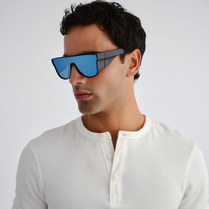 Man wearing futuristic sunglasses with a white shirt on a light gray background