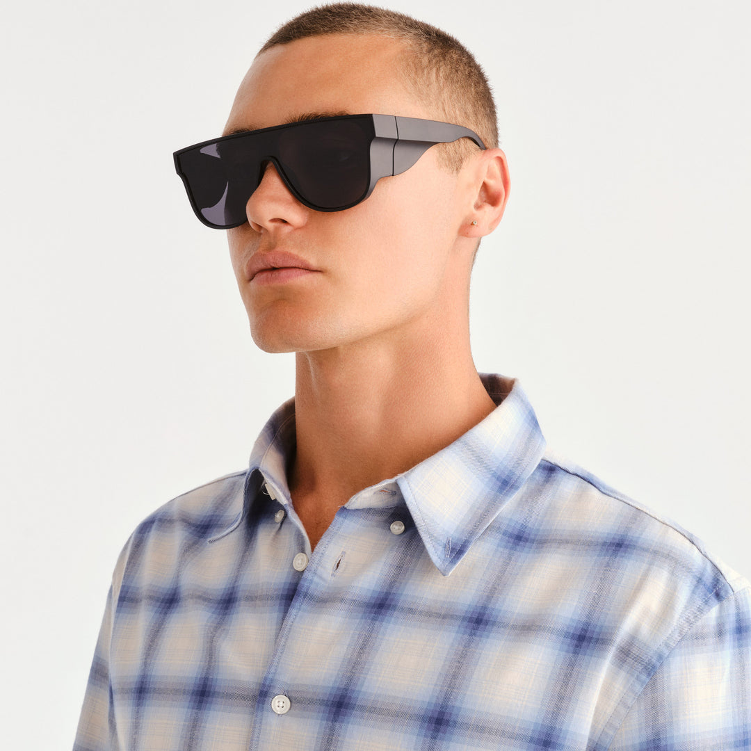 A man in profile wearing futuristic black shield-style sunglasses with dark lenses