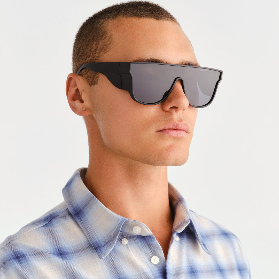 A man in profile wearing futuristic black shield-style sunglasses with dark lenses