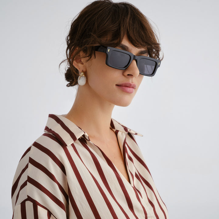 Woman wearing sunglasses and a striped shirt against a plain background
