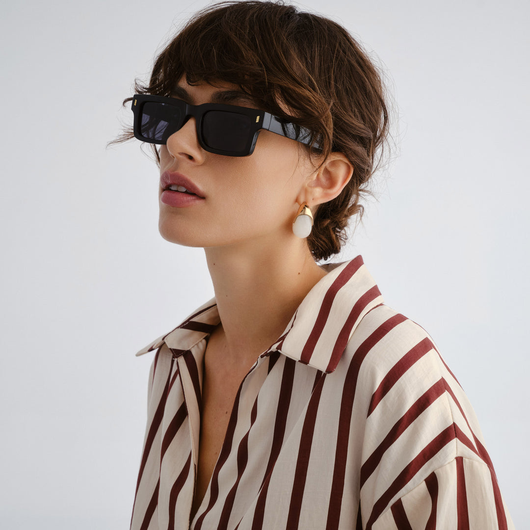 Woman wearing black sunglasses and a striped shirt on a plain background