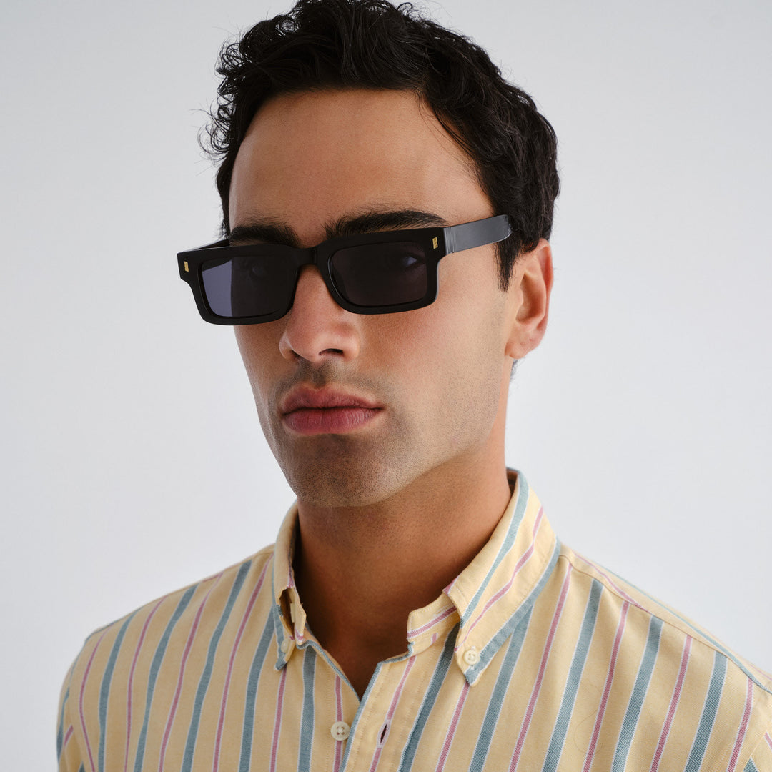 Man wearing black sunglasses and a striped shirt against a plain background