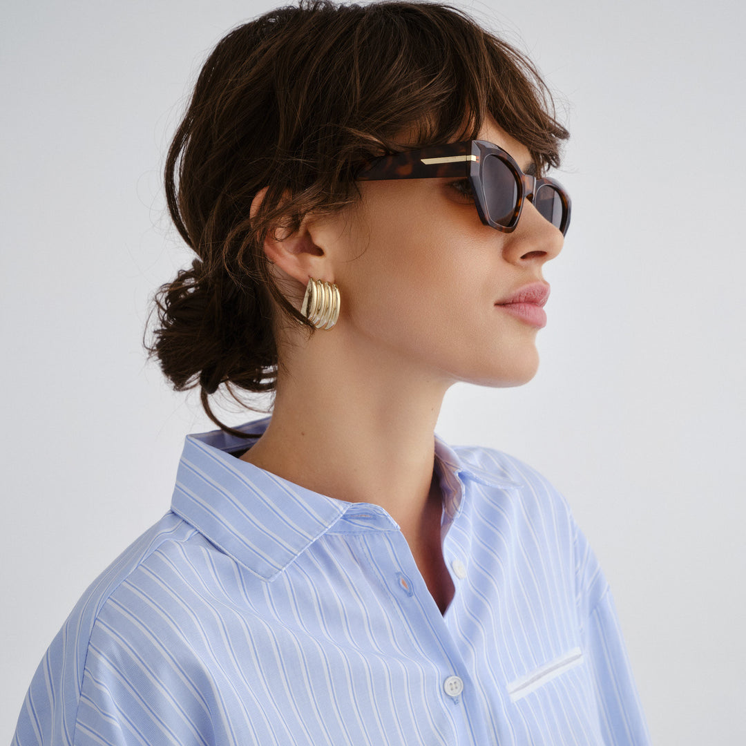 Woman wearing sunglasses and a light blue striped shirt against a white background