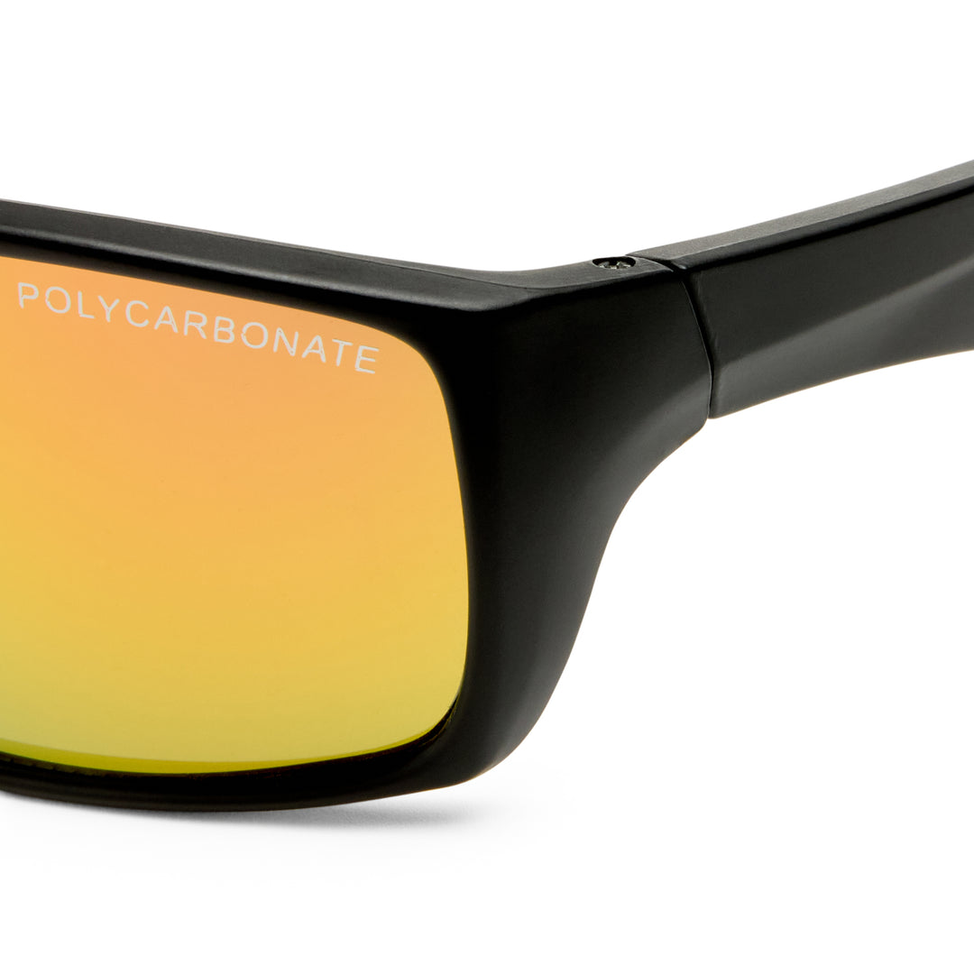 Close-up of a black sunglasses frame showing a yellow-to-orange mirrored lens with the word 'POLYCARBONATE' printed on it, against a white background.