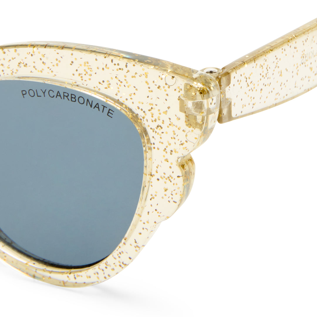 Close-up of a pair of sunglasses with a translucent cream acetate frame heavily speckled with gold glitter, paired with dark gray lenses.