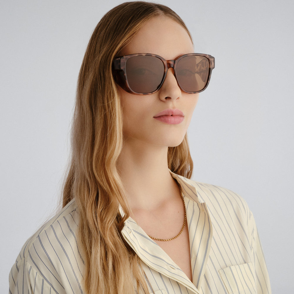 Woman wearing tort sunglasses with a neutral background